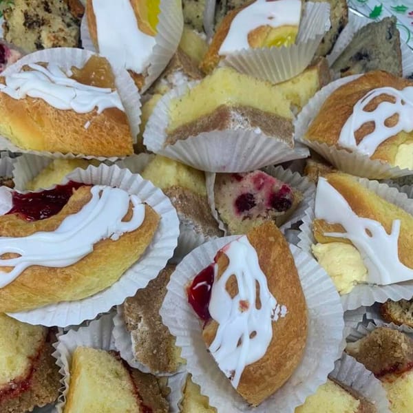 Assortment of pastries, including danishes with white icing and fruit fillings, and various cake slices.