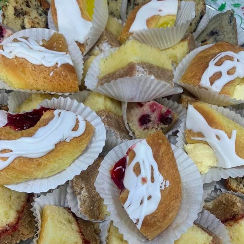 Assortment of pastries, including danishes with white icing and fruit fillings, and various cake slices.