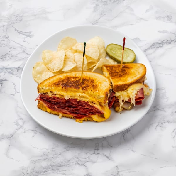 A grilled Reuben sandwich, cut in half, with chips and a pickle spear on a white plate.