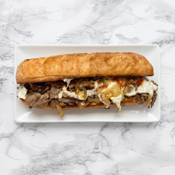 A delicious cheesesteak sandwich with melted cheese, onions, and sauce on a white plate.