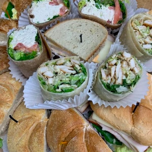 Assortment of sandwiches and wraps, including chicken Caesar wraps and deli sandwiches, arranged in a platter.