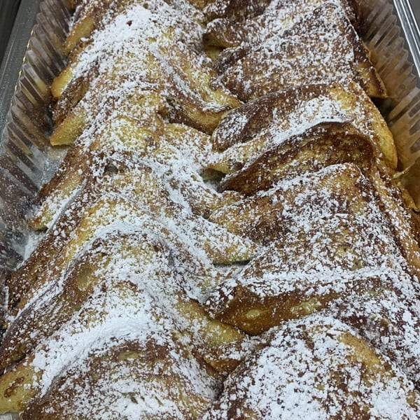 Golden French toast triangles, generously dusted with powdered sugar, arranged in a large serving tray.