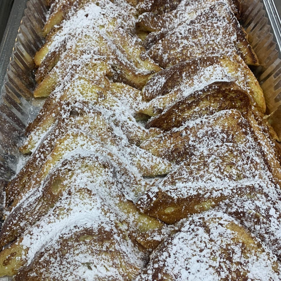 Golden French toast triangles, generously dusted with powdered sugar, arranged in a large serving tray.
